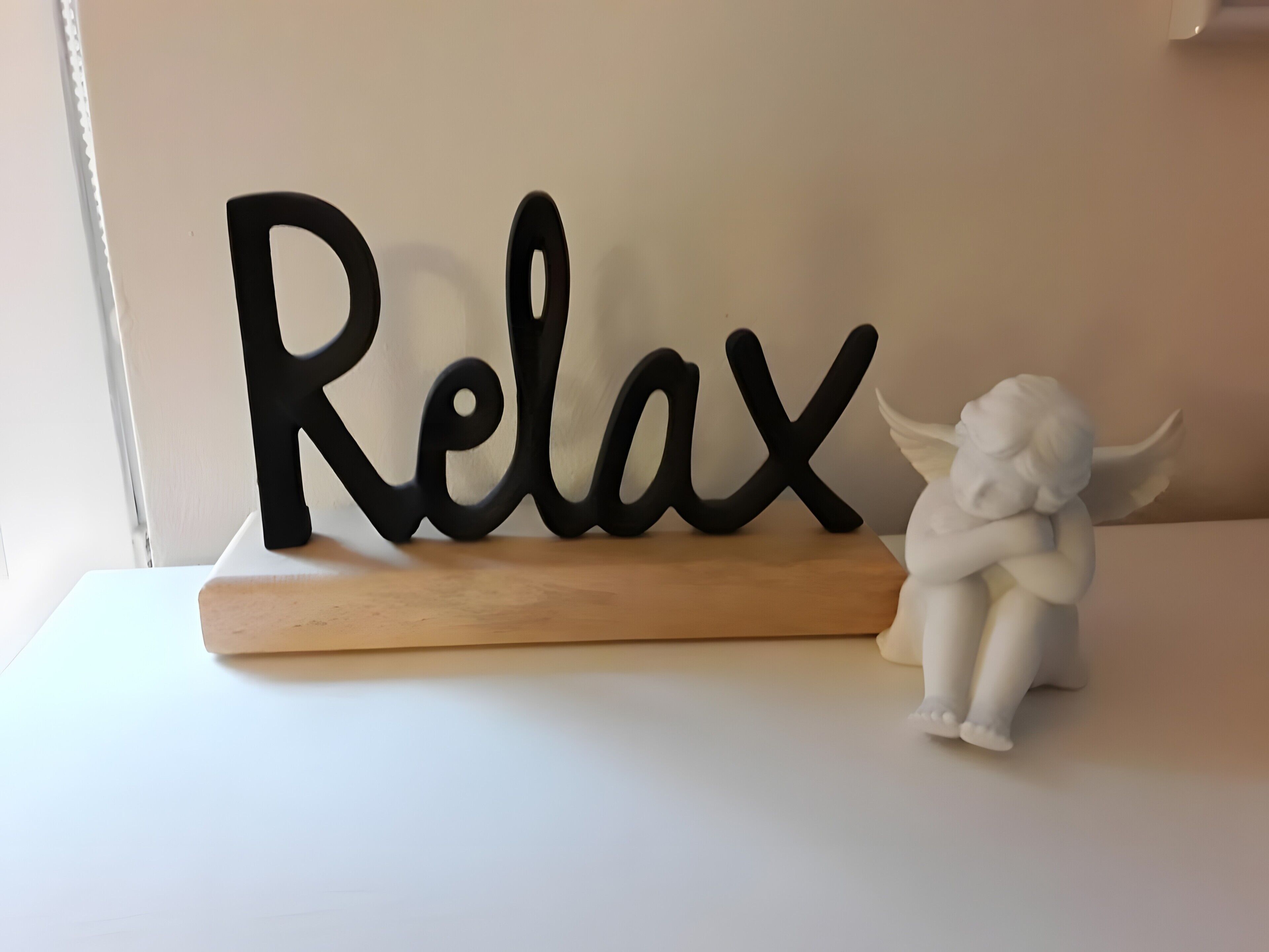 A decorative sign with the word 'Relax' on a wooden base, accompanied by a white angel figurine.