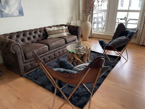 Ein Wohnzimmer mit einem braunen Ledersofa, einem Glastisch, einem flauschigen schwarzen Teppich und zwei Ledersesseln.
