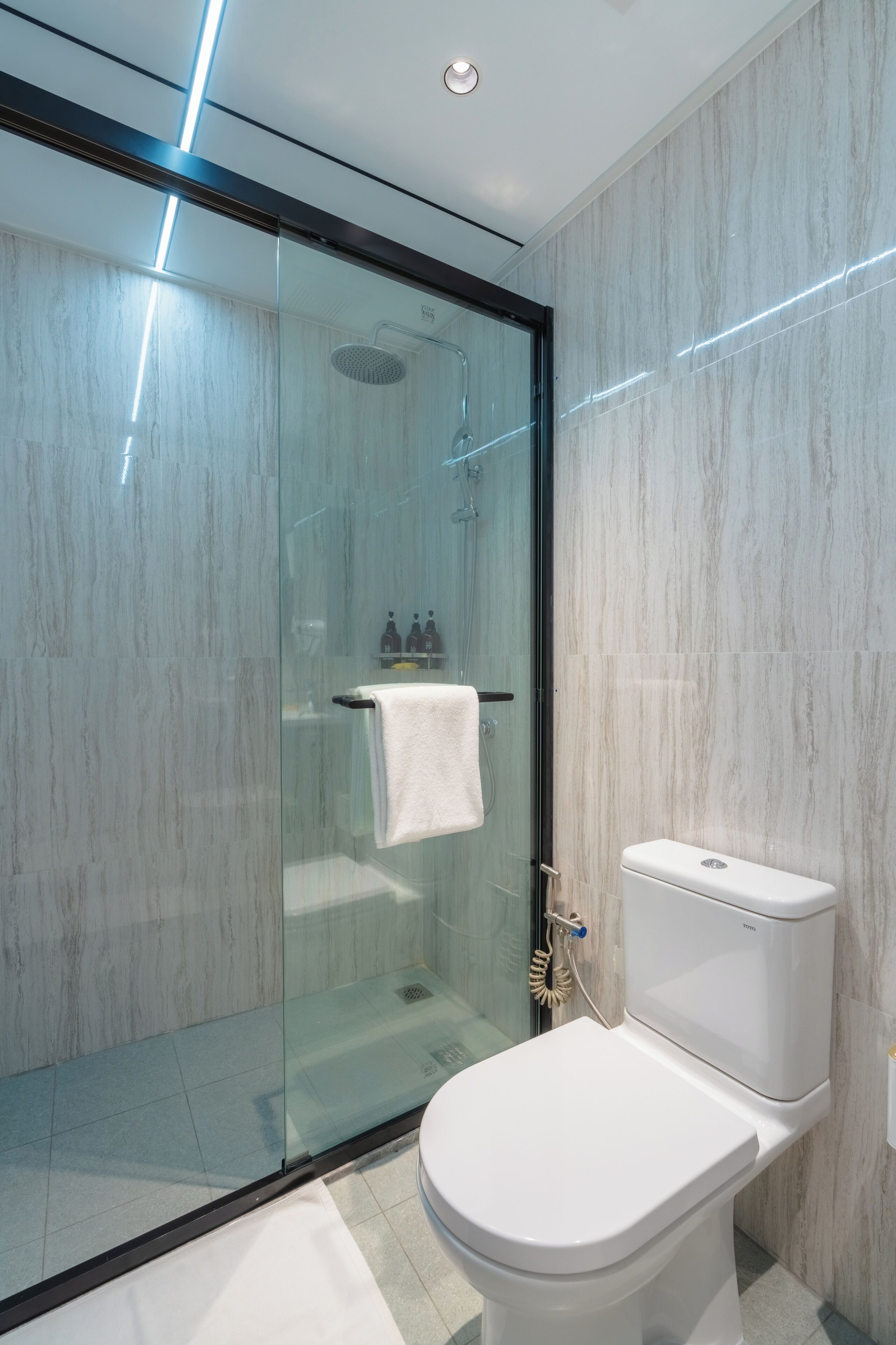 A modern bathroom with a glass-enclosed shower, a white toilet, and marble walls.