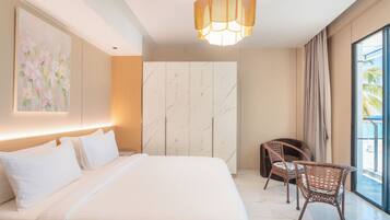 A modern hotel room with a large bed, a seating area with wicker chairs, a marble wall, and a large window with a view.