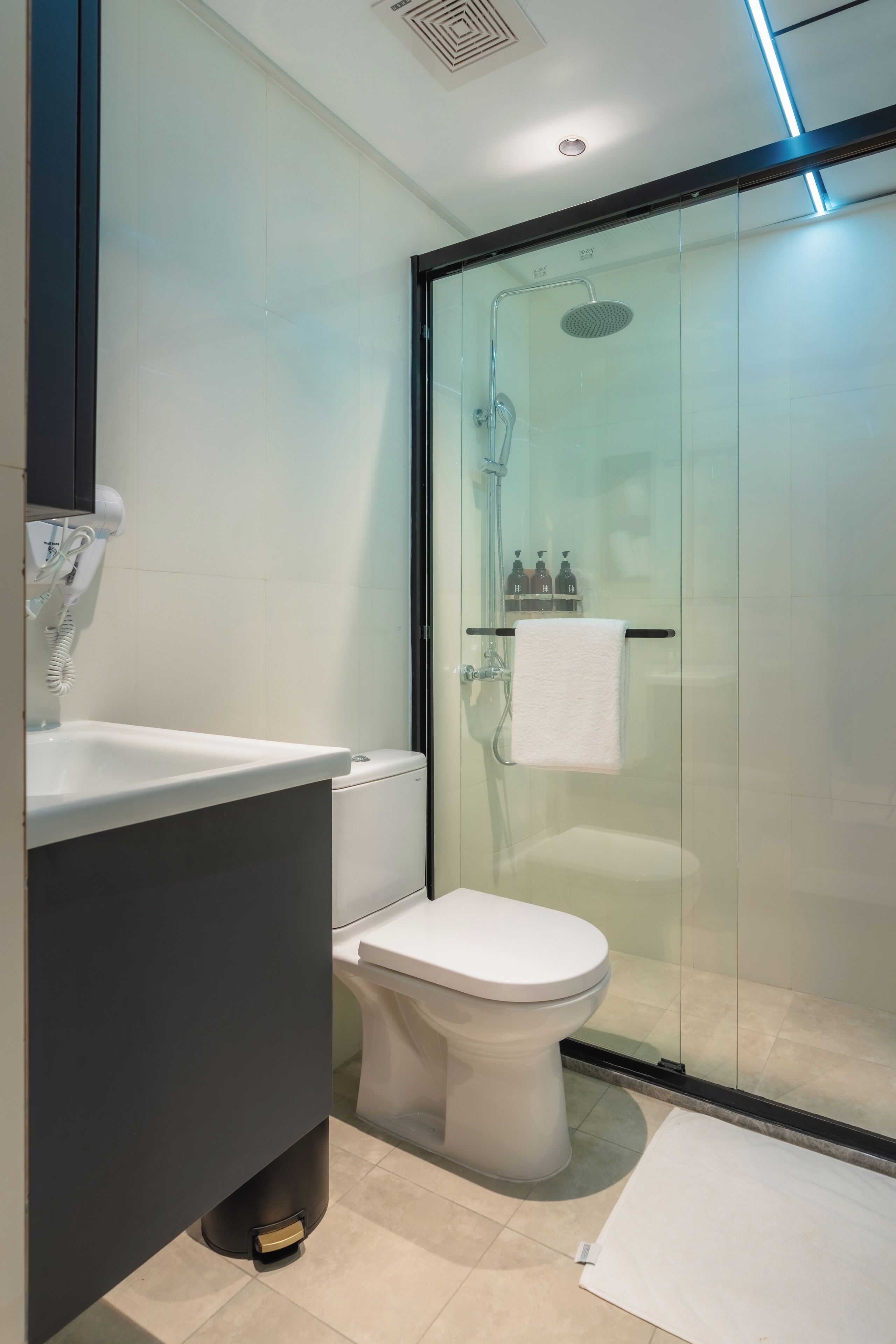 Un baño moderno con ducha envuelta en vidrio, inodoro blanco y lavamanos con gabinete oscuro.