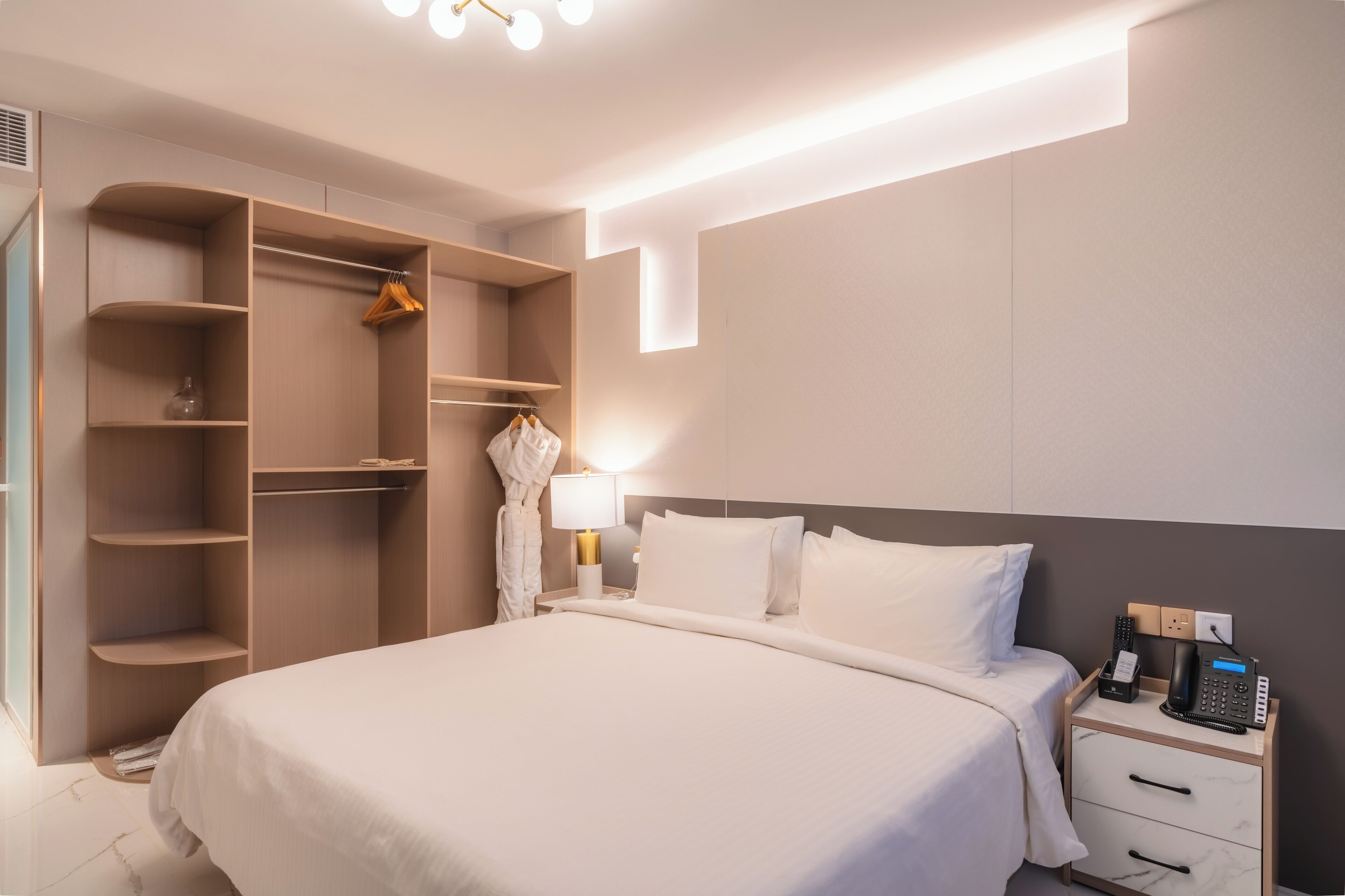 Et moderne hotelværelse med en stor seng, et walk-in closet, et natbord med lampe og en telefon.