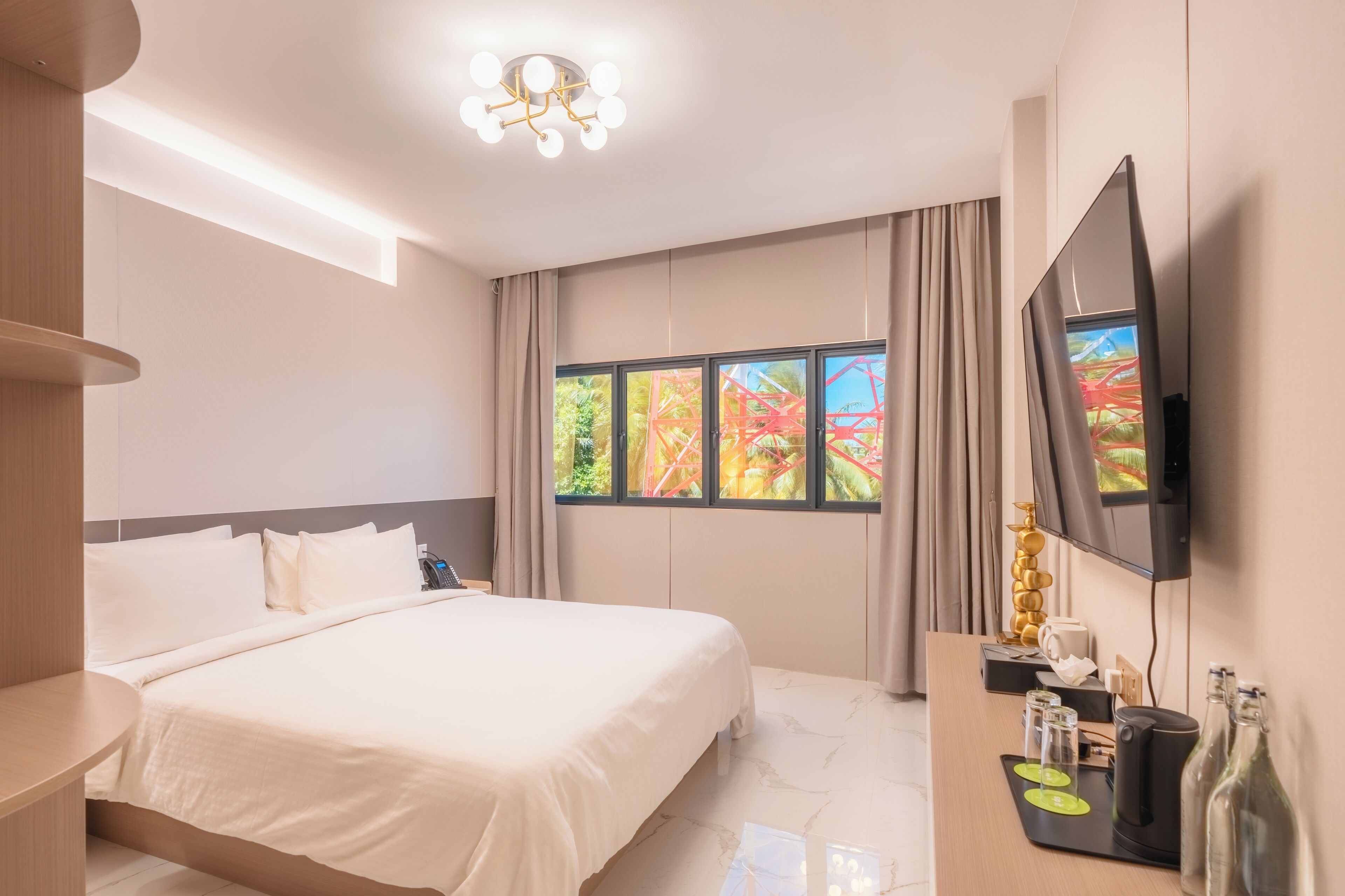 Hotelkamer met een bed, een bureau met koffiezetapparaat, een televisie en een raam met uitzicht op een kleurrijk pretpark.