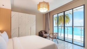 Quarto de hotel com cama, poltrona, janela grande com vista para a praia e oceano, e luminária pendente.