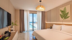 Quarto de hotel com uma cama grande, uma TV de tela plana, uma escrivaninha com cafeteira e vista para o mar através das portas de correr.