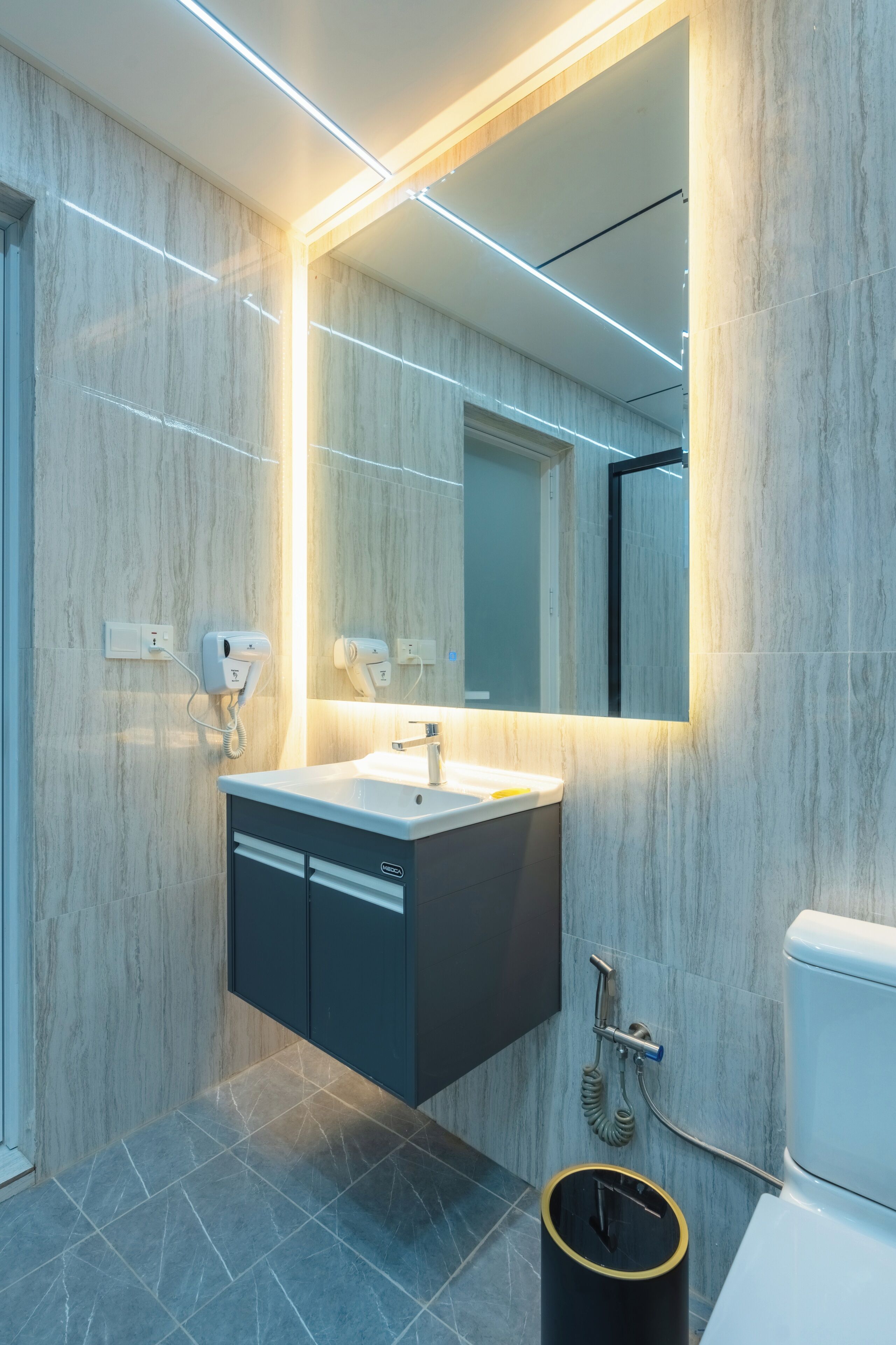 Un baño moderno con pared de mármol, lavamanos empotrado, espejo y retrete.
