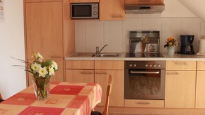 A compact kitchen with wooden cabinets, a microwave, a stove, and a sink. - Holiday Apartment 'A' with Balcony and Wi-Fi (Langenargen)