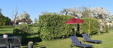 Un patio con dos sillones de descanso y una mesa, rodeado de un césped bien cuidado y un seto.