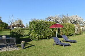 Un patio con dos sillones de descanso y una mesa, rodeado de un césped bien cuidado y un seto.