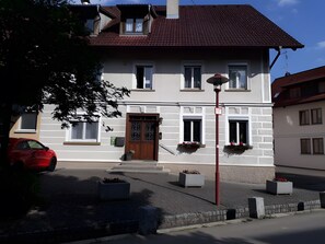 Ein zweistöckiges Gebäude mit rotem Ziegeldach, einem zentralen Eingang mit einer verzierten Tür und Fenstern in beiden Stockwerken.