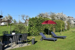 Eine Terrasse mit Tisch, Stühlen, einem roten Sonnenschirm und zwei Liegestühlen.