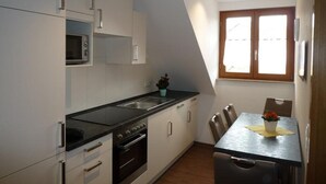 A compact kitchen with white cabinets, a black countertop, and a dining area with a table and chairs. - Apartment 'C' with Wi-Fi (Langenargen)