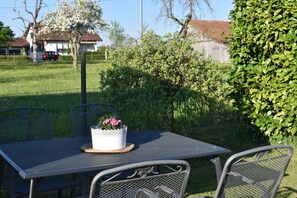 Ein Tisch aus Metall mit Stühlen im Freien, ein Blumenkorb und ein Zaun im Hintergrund.
