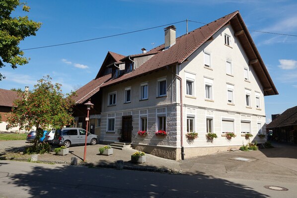 Ein zweistöckiges Gebäude mit geneigtem Dach und zahlreichen Fenstern, mit Blumenkästen im Erdgeschoss.