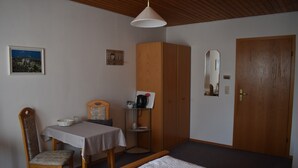 Ein Schlafzimmer mit einem Bett, einem Holzschrank, einem Tisch mit Stuhl, einem kleinen Regal und einem Spiegel an der Wand.