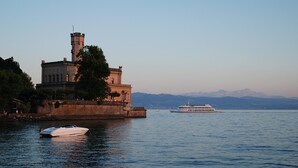 Ein historisches Gebäude mit einem Turm, ein Boot liegt in der Nähe und ein großes Kreuzfahrtschiff ist in der Ferne zu sehen.