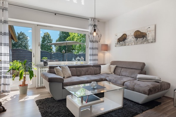 A modern living room with a sectional sofa, a glass coffee table, and a large window offering a view of the outdoors.