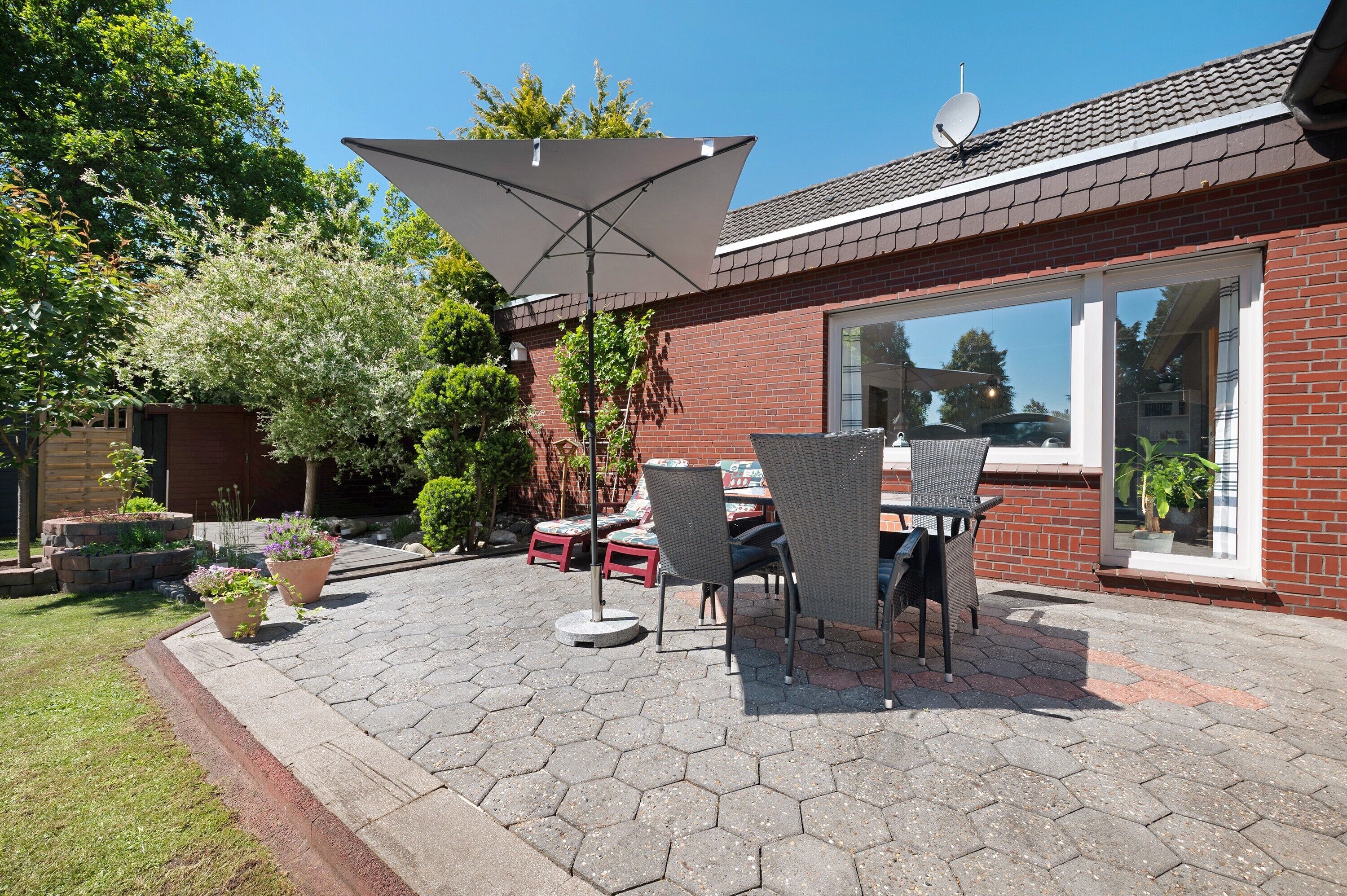 En terrasse med sekskantede fliser, udendørs møbler og en stor parasol.
