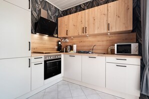 A modern kitchen with white cabinets, a wooden countertop, a microwave, an oven, and a sink.