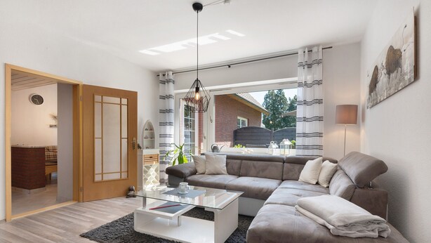 Una sala de estar moderna con un sofá seccional, una mesa de centro de vidrio y vistas amplias por ventanas grandes.
