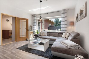 A modern living room with a sectional sofa, a glass coffee table, and a view through large windows. - Apartment 'Wilma Spetzerfehn' with Private Terrace, Private Garden (Großefehn)