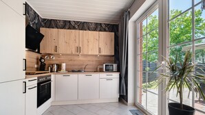 Una cocina moderna con armarios blancos, horno negro, microondas y un amplio ventanal con vistas a árboles.