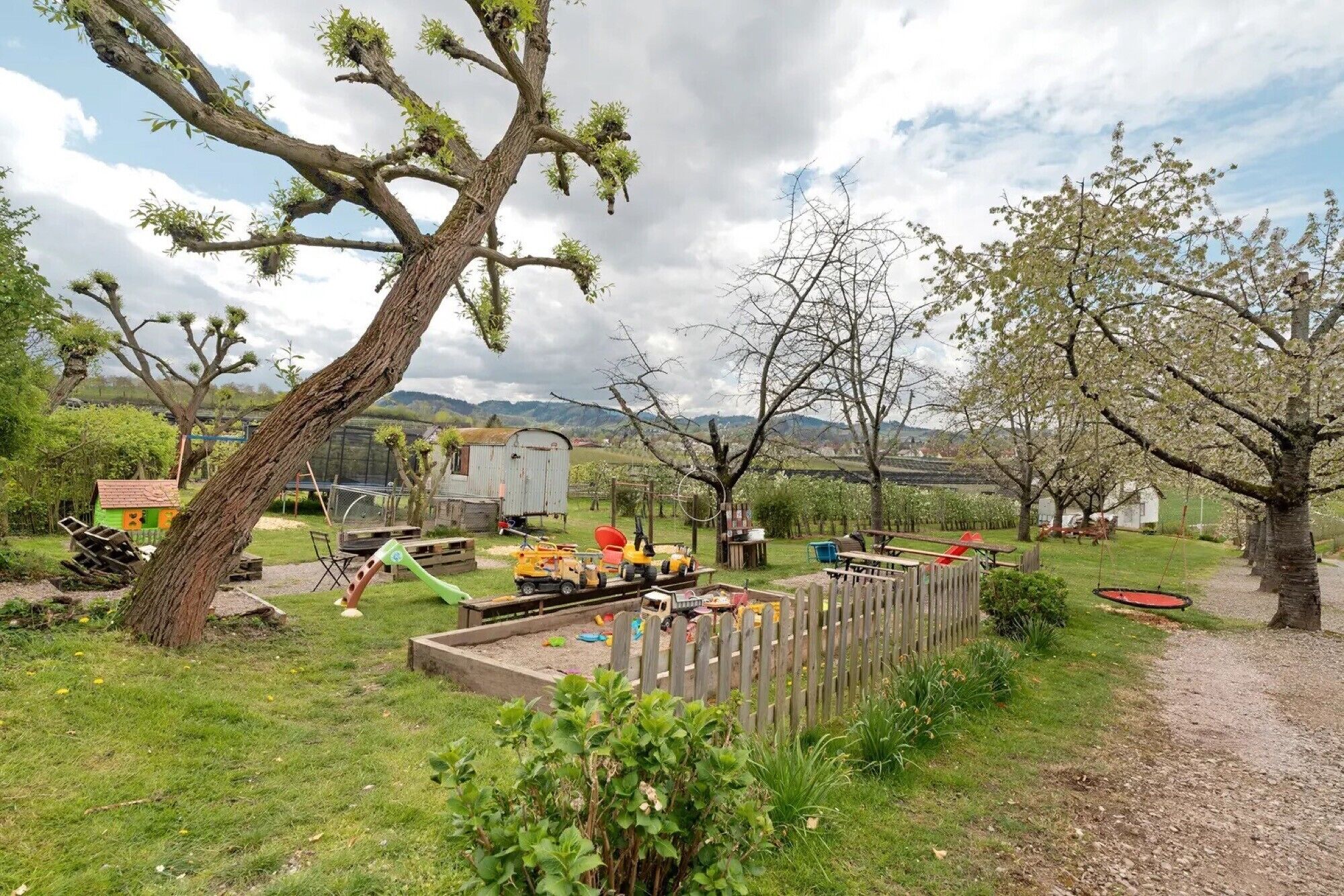 A rural outdoor setting with a dirt path, wooden play structures, and a tractor.