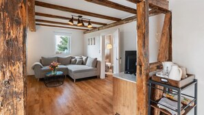 A living room with a grey sofa, wooden beams, a round coffee table with flowers, and a TV stand with a kettle.