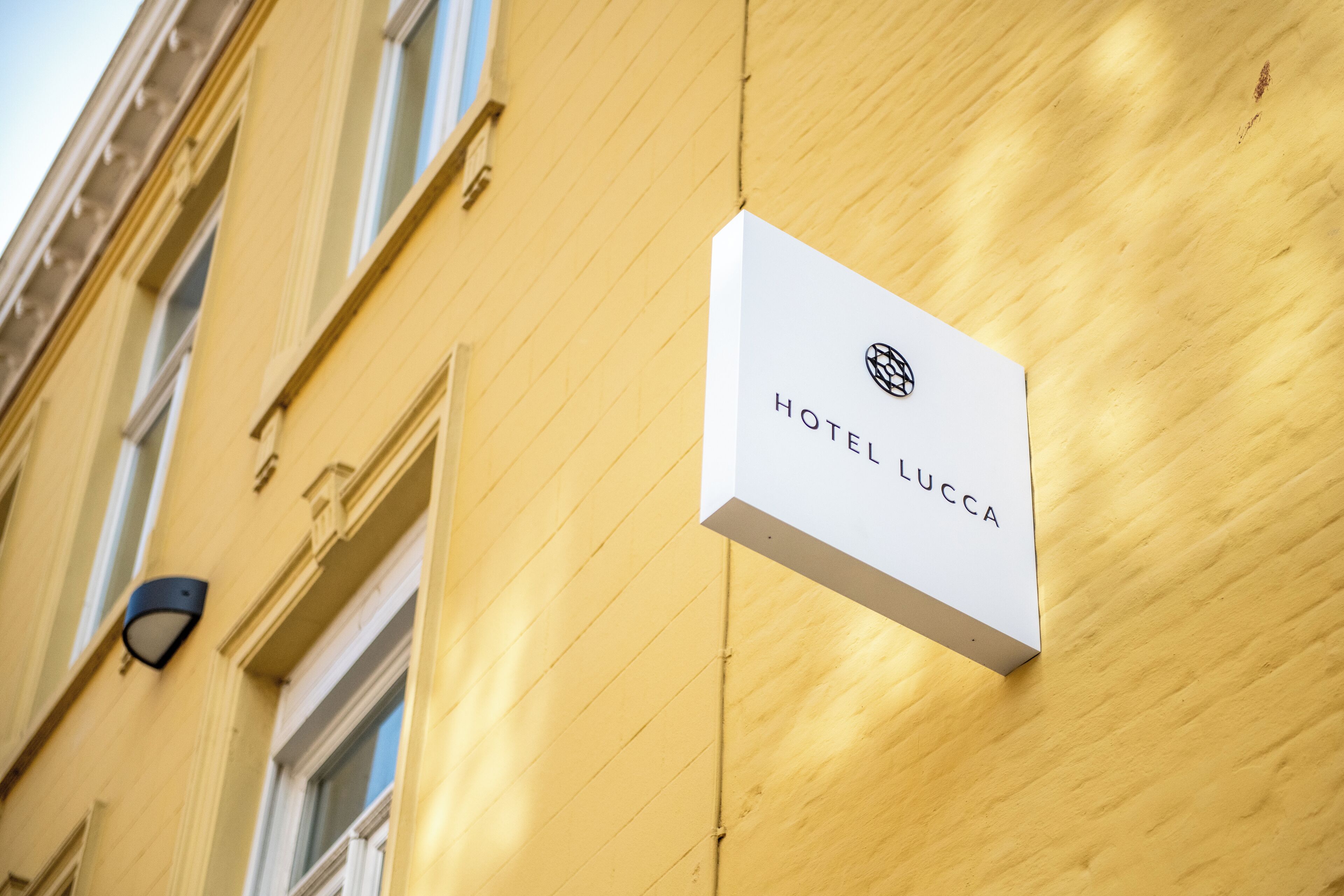 Une enseigne blanche portant l’inscription « HÔTEL LUCCA », fixée sur la façade jaune d’un immeuble.