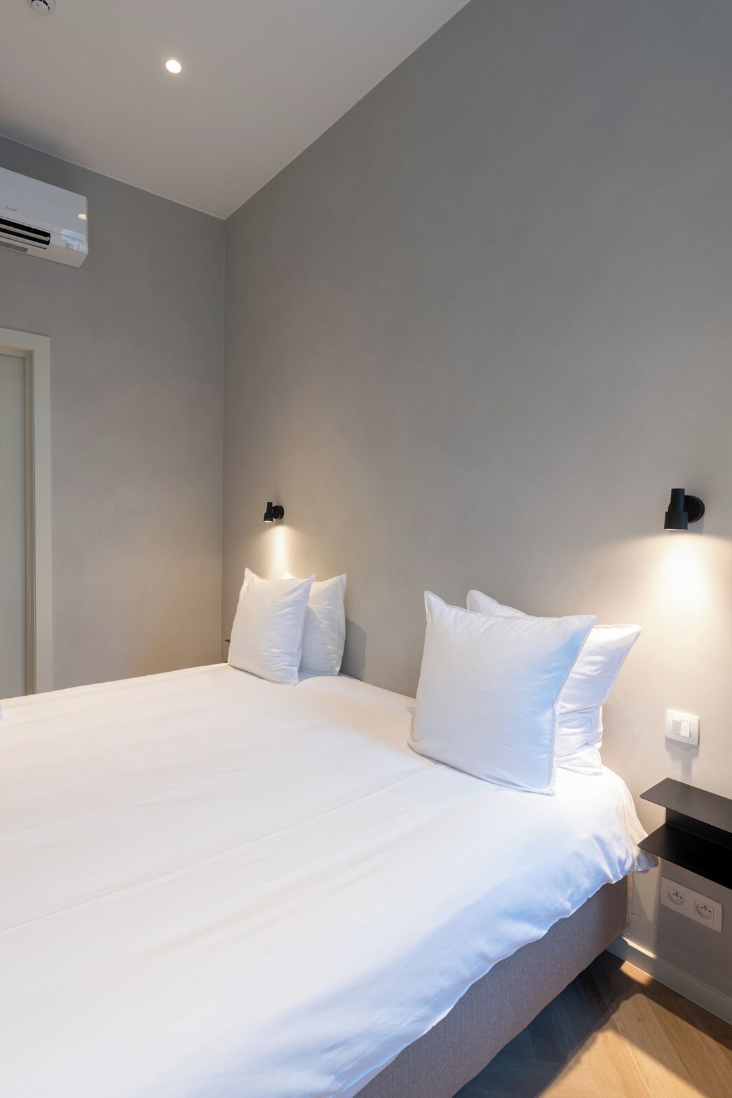 A modern hotel room with a large bed, two bedside tables, and a wall-mounted air conditioner.