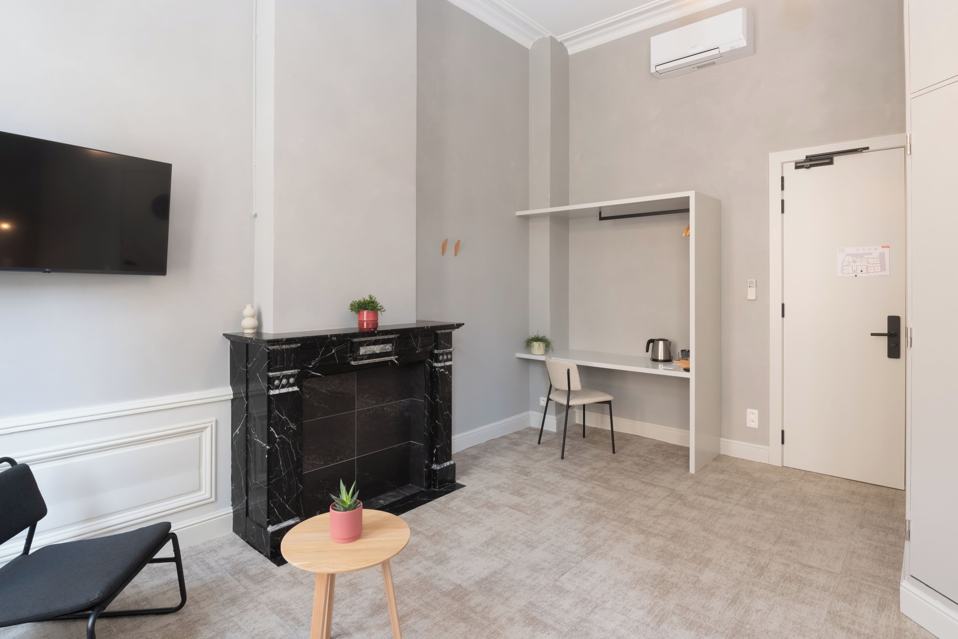 Una habitación moderna con televisor de pantalla plana, chimenea de mármol negro, una mesita redonda con una planta, una silla negra y una puerta blanca.