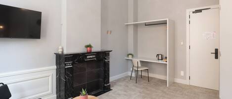 Una habitación moderna con televisor de pantalla plana, chimenea de mármol negro, una mesita redonda con una planta, una silla negra y una puerta blanca.