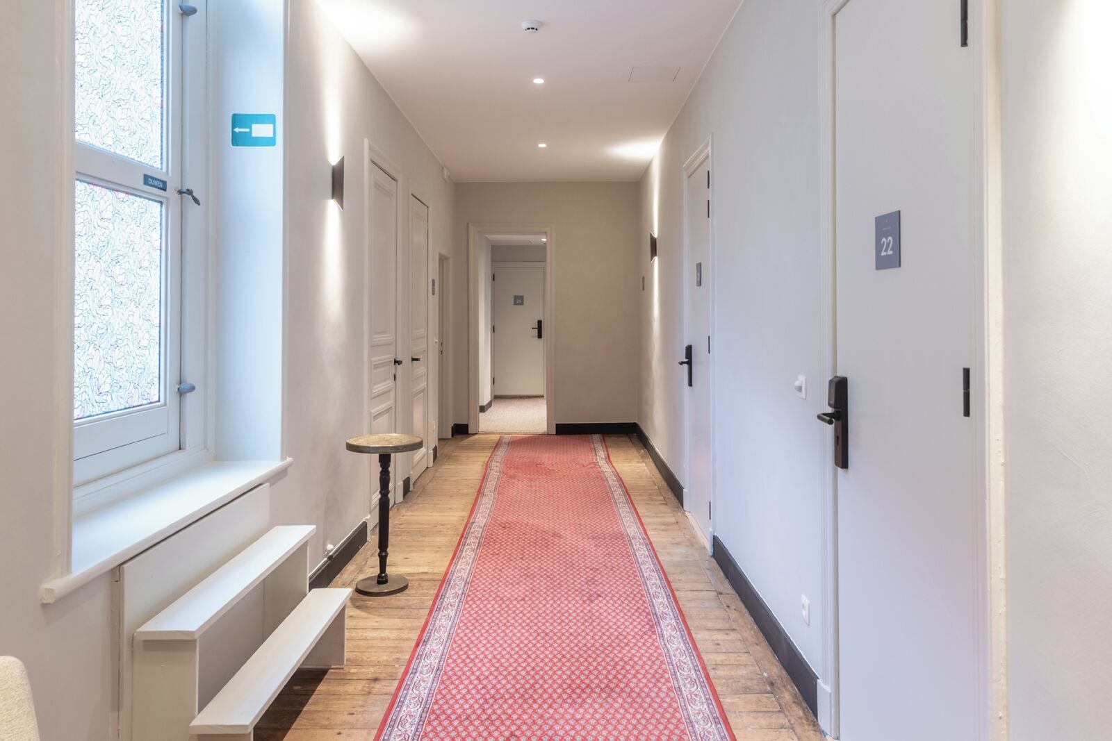 Pasillo de hotel con alfombra roja, paredes blancas y puertas numeradas 22.