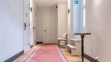 A hallway with a red patterned carpet, a white door, a chair, and a small table with a lamp.