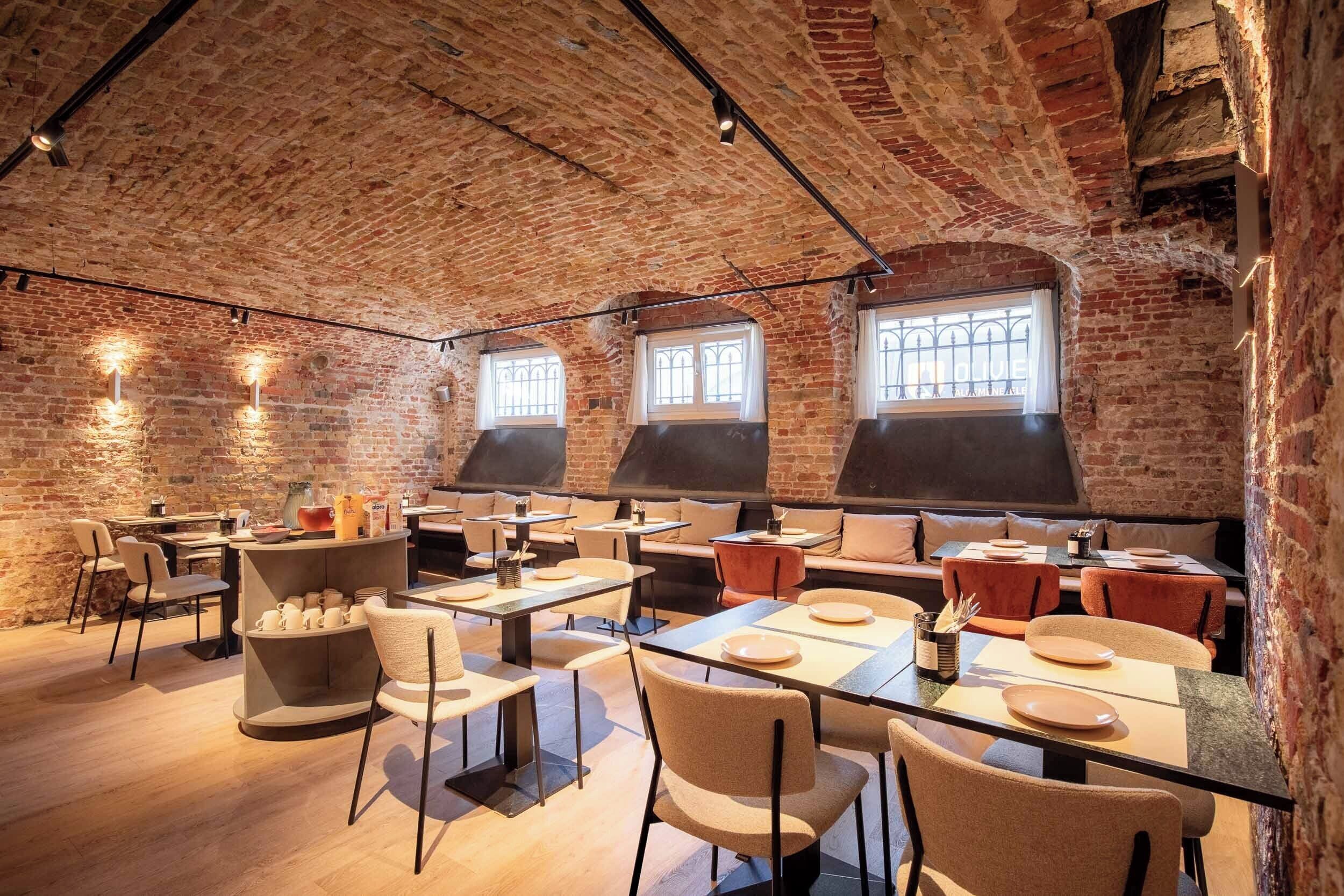 A restaurant with brick walls, large windows, and a mix of table and booth seating.