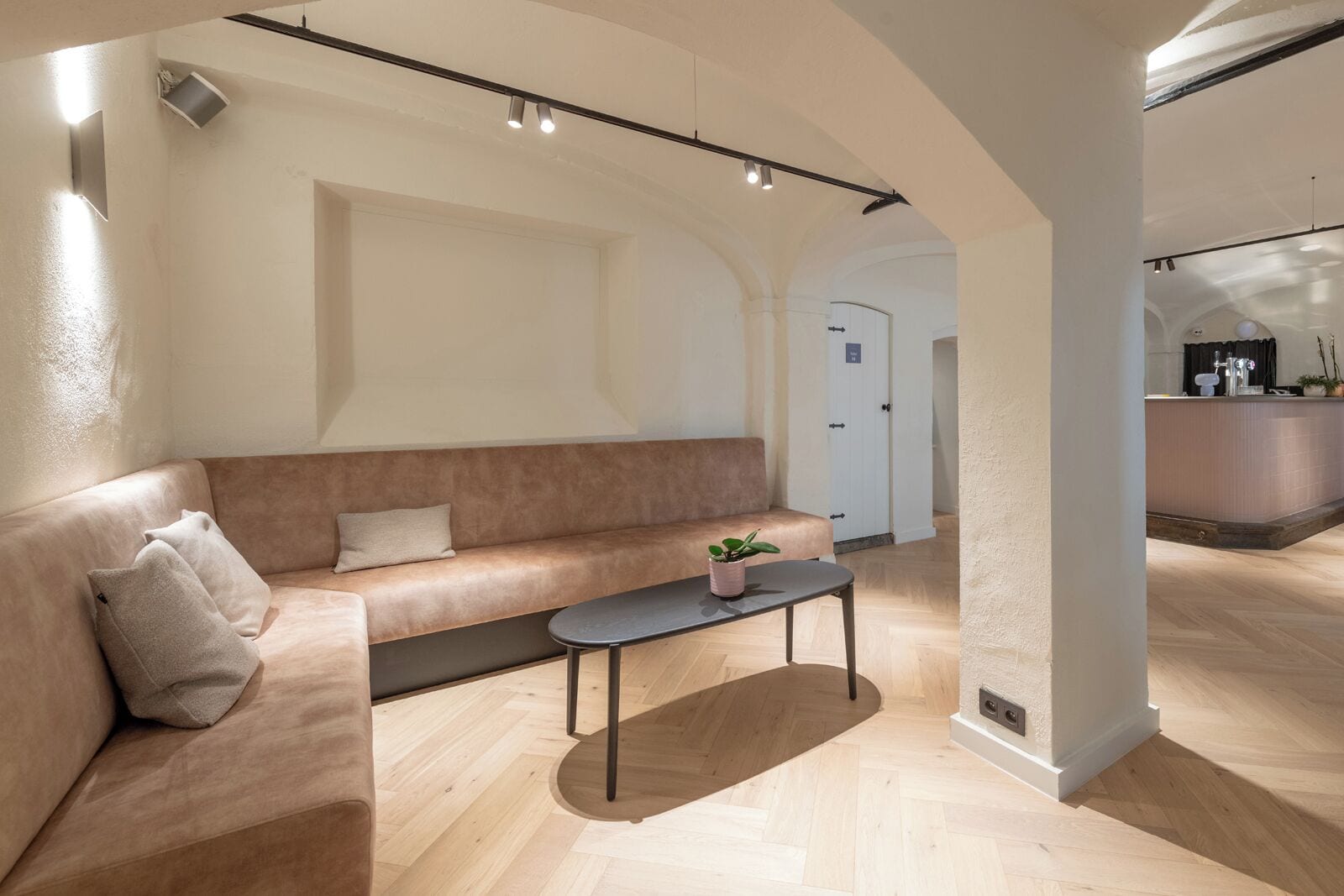 Une chambre d’hôtel moderne avec un canapé beige, une petite table sur laquelle est posée une plante, et un comptoir de réception en arrière-plan.