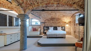Un dormitorio con techo de ladrillo, una cama, una mesita de noche, una silla y una ventana.