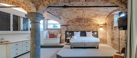 A bedroom with a brick ceiling, a bed, a nightstand, a chair, and a window.