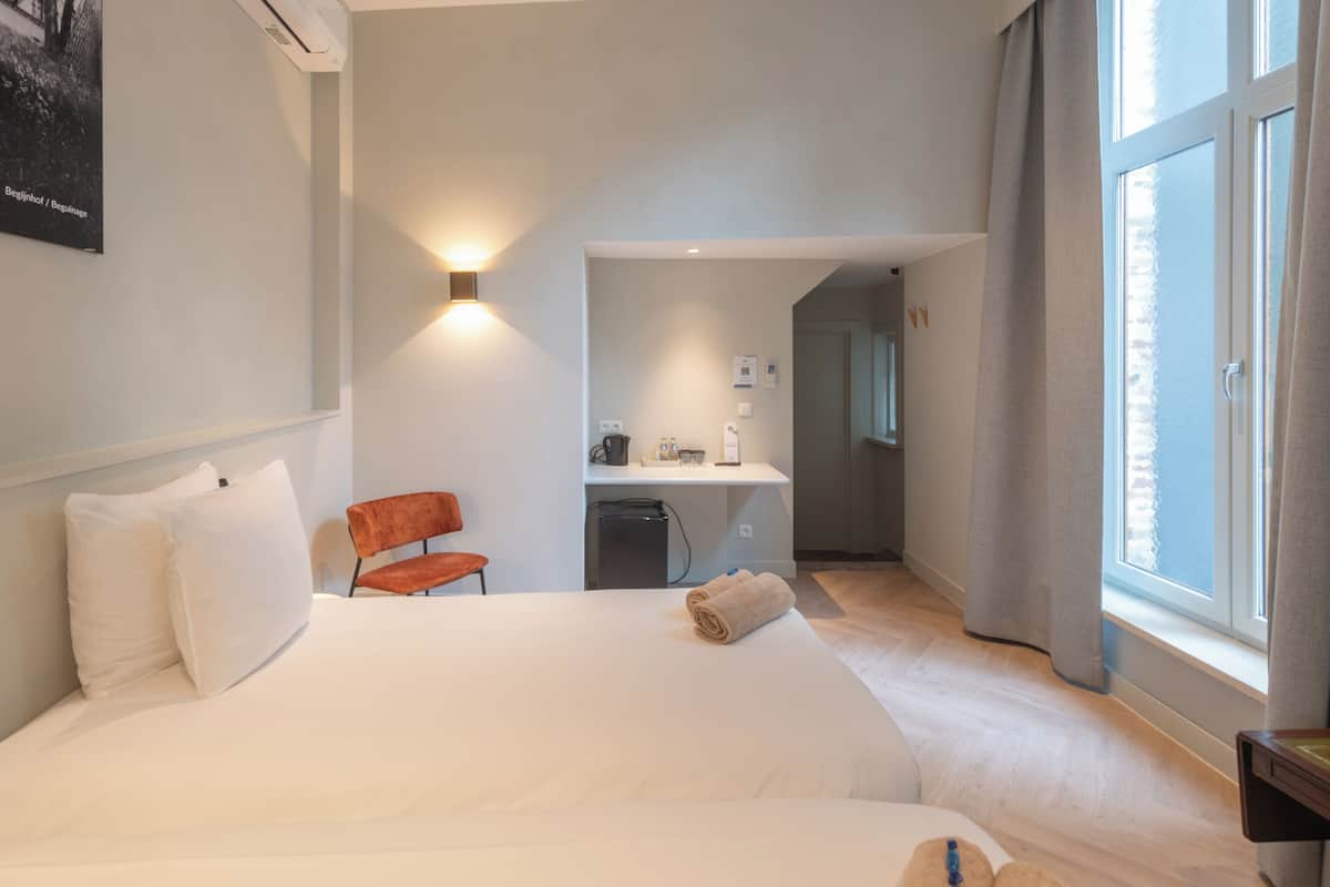 A hotel room with a bed, a desk, a chair, and a window.