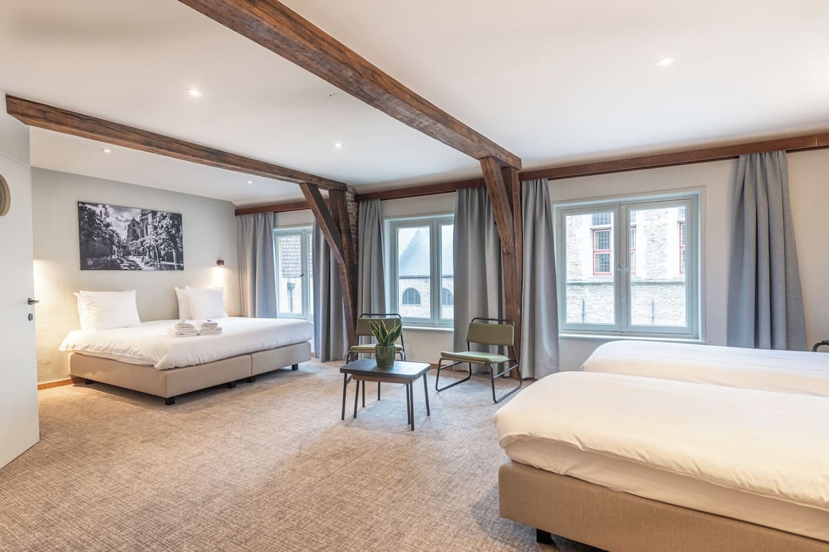 A hotel room with two beds, a small table with a plant, and large windows with curtains.