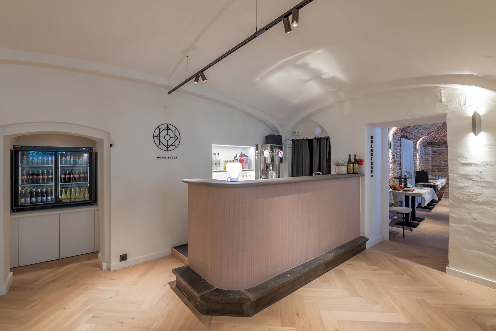 A hotel lobby with a reception desk, a refrigerator with beverages, and a brick wall.