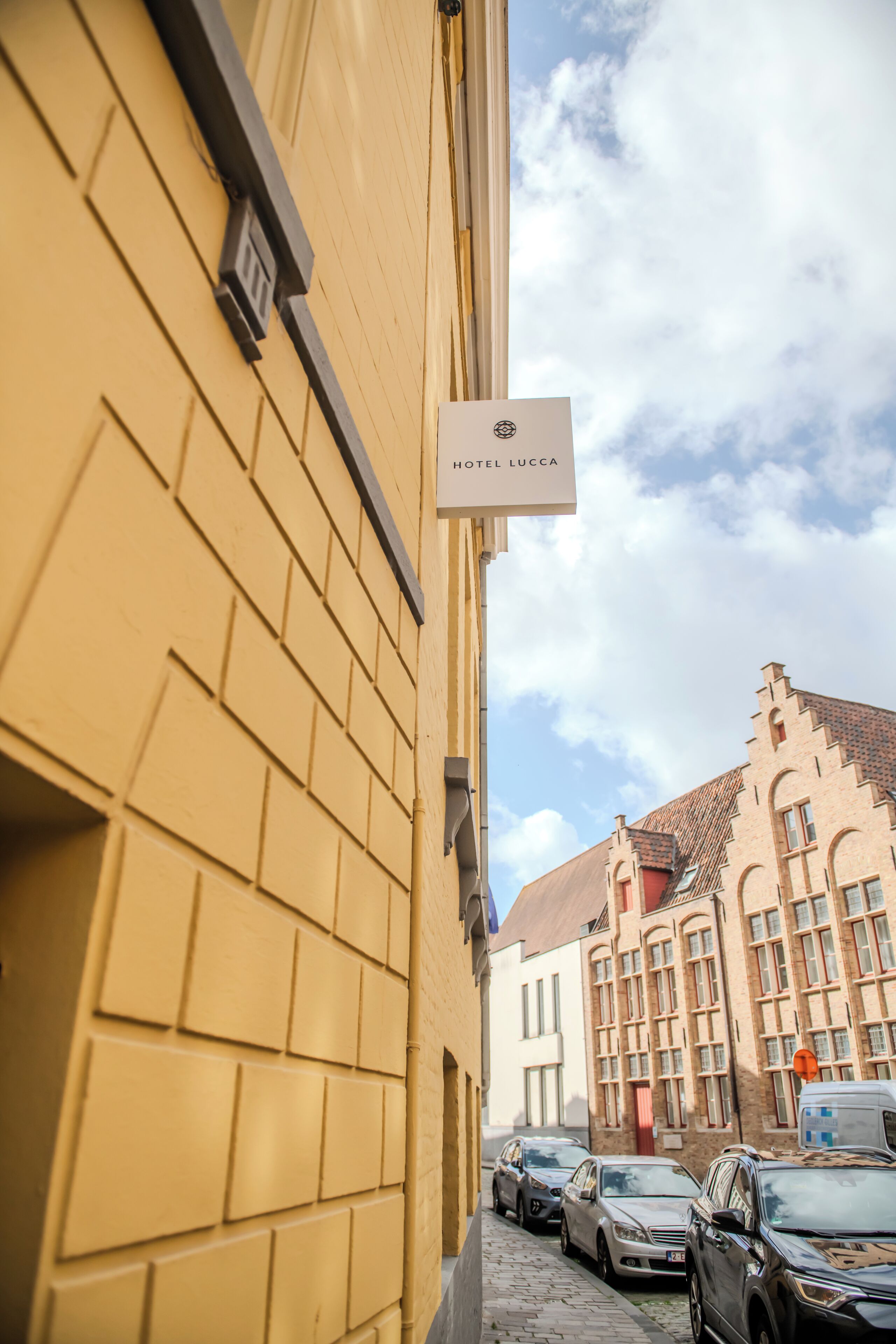 Una calle estrecha con coches aparcados y un edificio con un cartel que dice 'HOTEL LUCCA'.