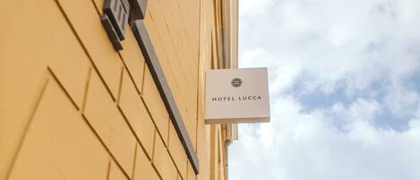 Una calle estrecha con coches aparcados y un edificio con un cartel que dice 'HOTEL LUCCA'.