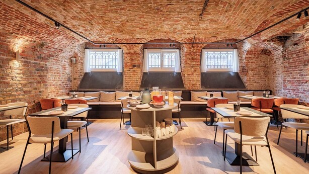 Comedor de paredes de ladrillo con mesas y sillas, un mostrador central de servicio y tres ventanas.