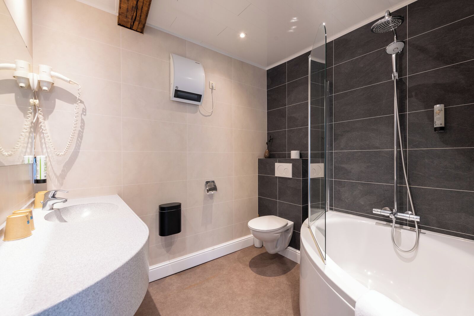 A modern bathroom with a freestanding bathtub, a glass-enclosed shower, a toilet, and a vanity with a sink and hairdryer.