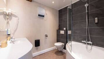 Een moderne badkamer met een vrijstaand bad, een douche met glazen wanden, een toilet en een wastafel met een wasbak en haardroger.