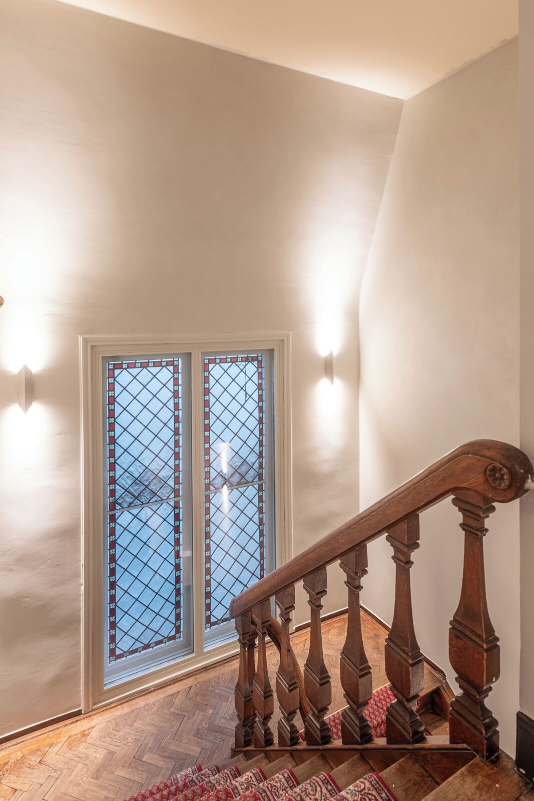 A wooden staircase with a handrail, a patterned rug, and a window with a grid design.