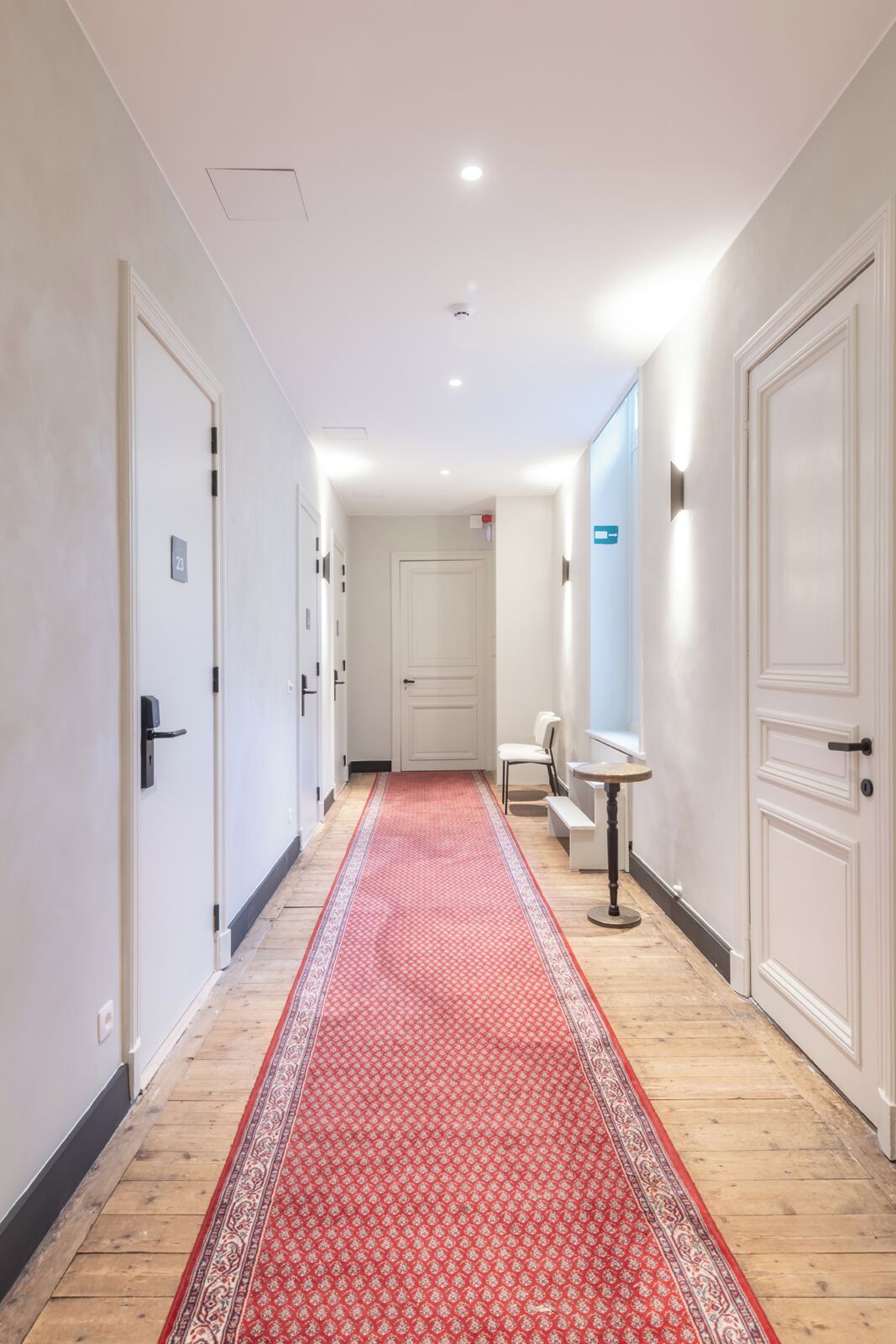 A hallway with a red patterned carpet, white doors, and a small table with a chair.