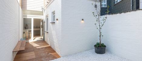 Een smalle steeg met een houten terras, witte muren en een plant in pot.