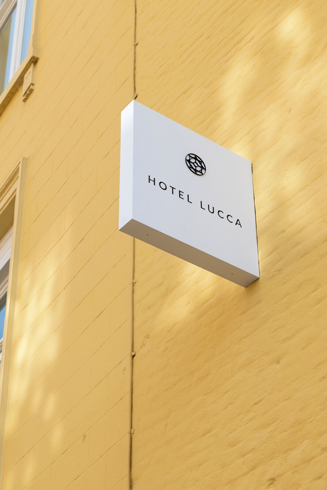 A hotel sign labeled "HOTEL LUCCA" mounted on a yellow building.